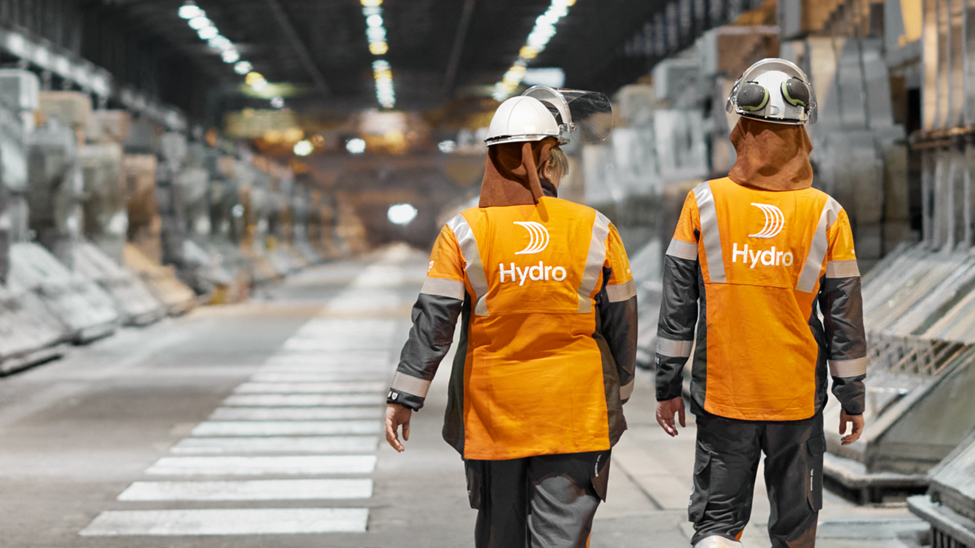 a couple of men wearing safety vests and helmets walking down a street
