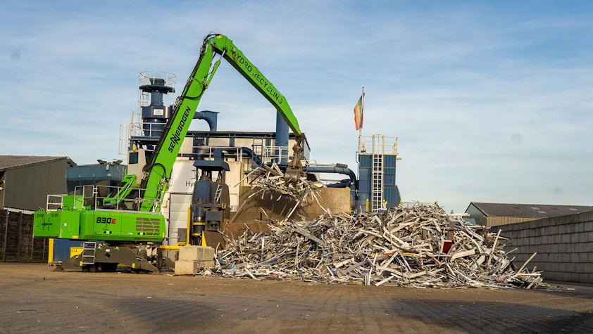 a green machine in front of a pile of scrap metal