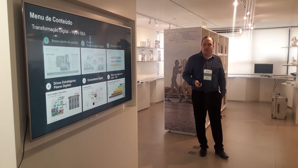 Daniel, de pé, apontando para a tela onde está sua apresentação, durante a palestra na Abal